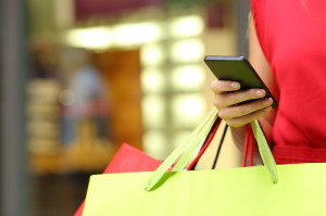 44895703 - shopper woman hand shopping with a smart phone and carrying bags