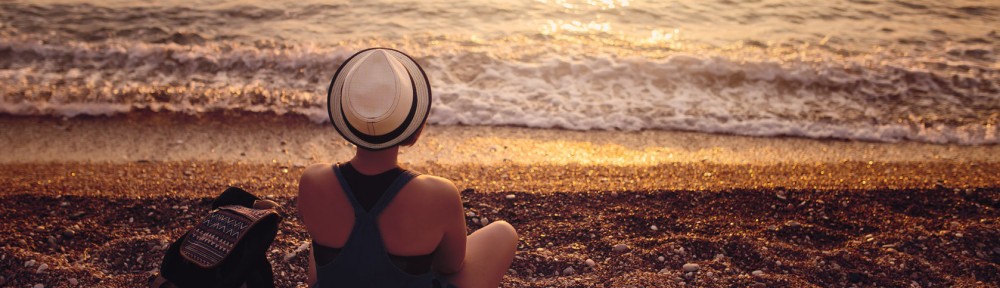 65379899 - woman sitting on pebble coast near sea at sunset