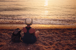 65379899 - woman sitting on pebble coast near sea at sunset
