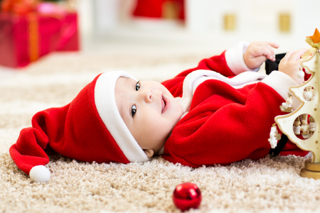 Happy Smiling baby lying on back wearing Christmas Santa hat and suit