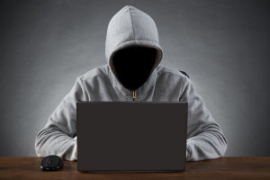 45165795 - hacker in hood jacket using laptop at table