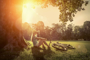 46573937 - woman sitting under sun light at day near her bicycle in the park