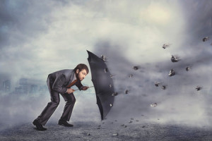 39183857 - business man protects himself from rocks with umbrella over grey