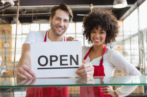 46212604 - smiling team posing behind the counter with open sign at the bakery