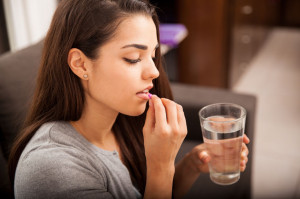 33909710 - cute young brunette taking a pill with a glass of water at home