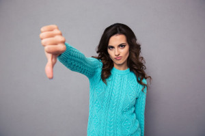 47293656 - portrait of a young woman showing thumb down over gray background