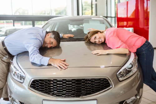 Casual smiling couple hugging their new car at new car showroom