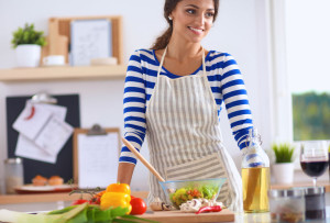 49568447 - smiling young woman  mixing fresh salad, standing