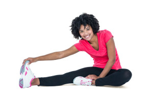 Portrait of young woman touching toes while exercising against white background