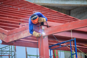Risky welder while climbing and welding on top of the steel roof structure work at the building construction site. Skilled worker is welding on the high steel structure at the construction project.