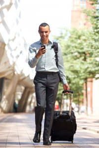 Full body traveling businessman walking in city with suitcase and mobile phone