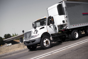 White semi truck and stainless steel refrigerator trailer on hig