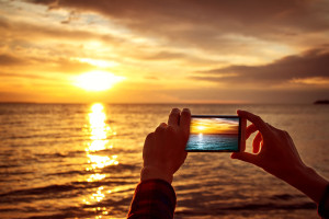 hands holding mobile phone at sunset