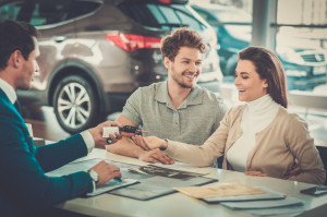 Salesman giving the key of the new car to a young couple at the
