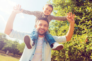 We like spending time together! Low angle view of happy little boy stretching out hands while his father carrying him on shoulders