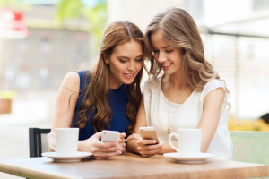 women with smartphones and coffee at outdoor cafe