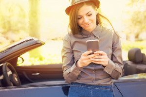 Successful woman standing by her car texting on mobile phone