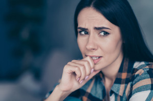 Close up side profile photo she her lady displeased hopeless arm hand bite fingers nerves made mistake have doubts tell or no wear checkered plaid shirt sit lean divan flat house living room indoors