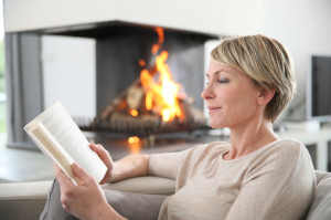 Middle-aged woman reading book by fireplace