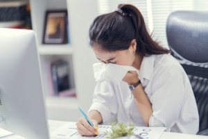 Women are sneezing and are cold. She is in the office.