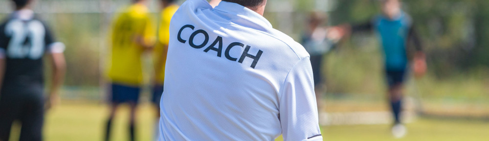 Back of sport coach wearing COACH shirt at an outdoor sport fiel