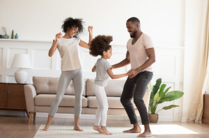 Happy funny active african family with daughter dancing at home