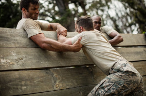 Soldiers helping man to climb wooden wall