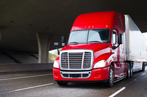 Bright red modern big rig semi truck with dry van trailer runnin