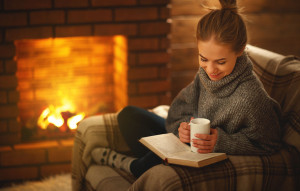 young woman   reading a book by the fireplace on a winter evening