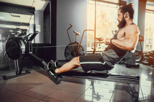 Muscular fit man using rowing machine at gym