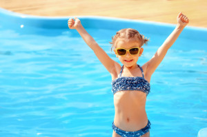 little cute girl holding hands up near a swimming pool
