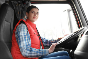 Young female driver sitting in cabin of big modern truck