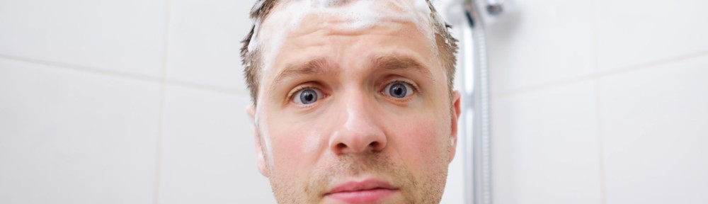 Worried caucasian foamed young man after the water in the shower was turned off, looking at the camera.