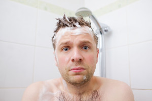 Worried caucasian foamed young man after the water in the shower was turned off, looking at the camera.