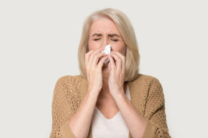 Ill allergic old woman blowing runny nose isolated on background