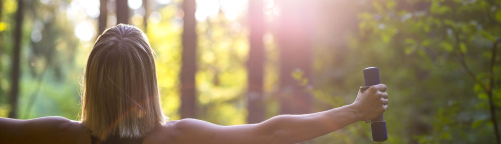 Young blonde woman working out with dumbbells in beautiful natur
