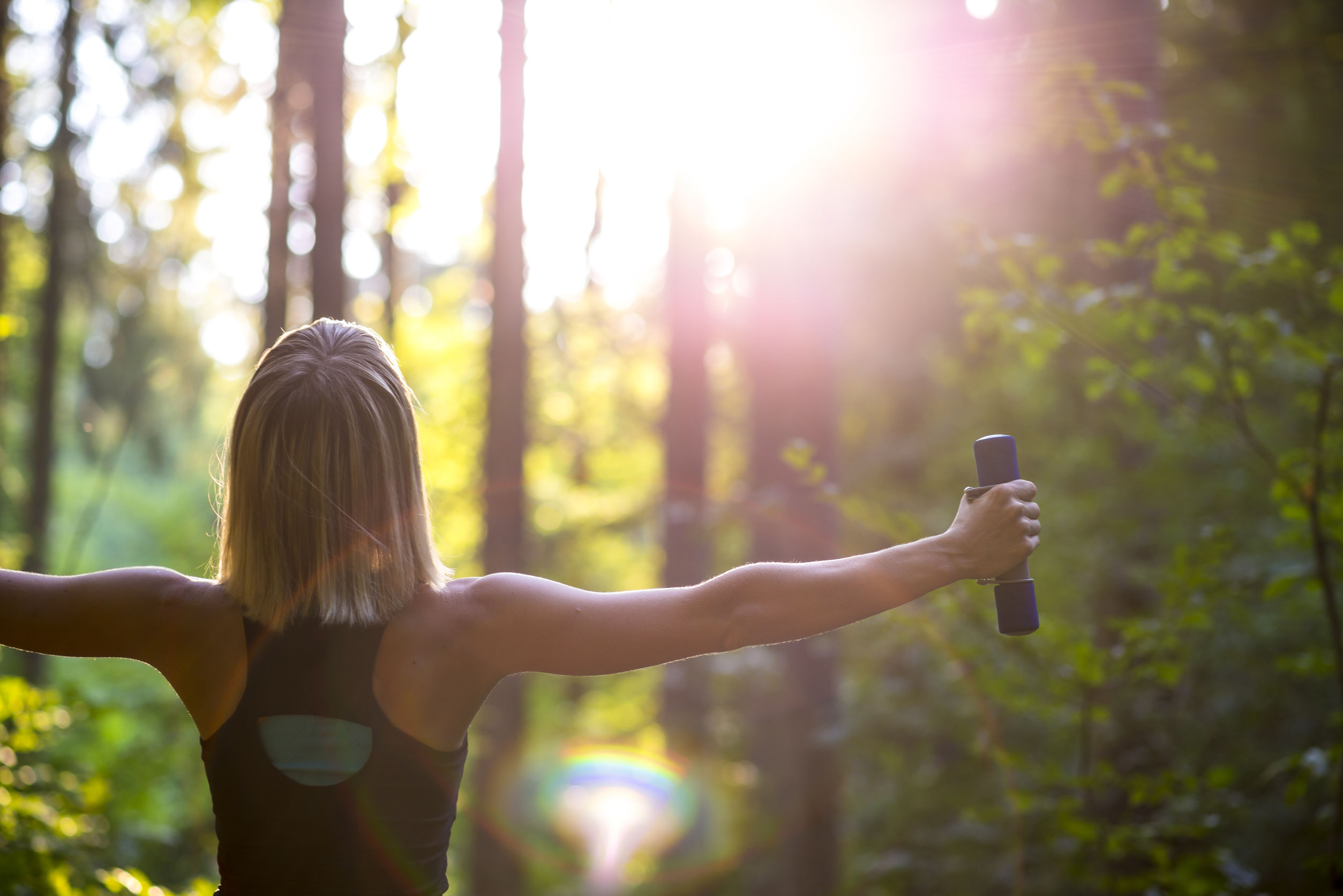 Young blonde woman working out with dumbbells in beautiful natur