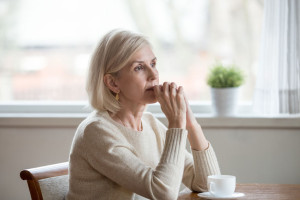 Thoughtful woman sitting at table with cup of tea