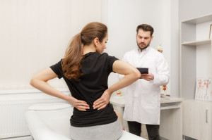 Male doctor examining female patient suffering from back pain. Medical exam. Chiropractic, osteopathy, post traumatic rehabilitation, sport physical therapy. Alternative medicine, pain relief concept