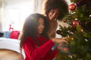 Mother And Daughter Hanging Decorations On Christmas Tree At Home