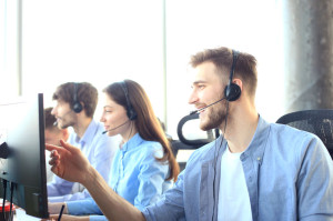 Portrait of call center worker accompanied by his team. Smiling customer support operator at work.