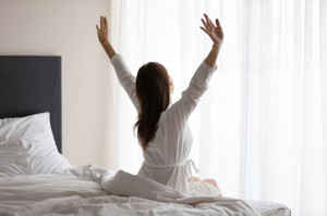 Happy young woman stretching waking up sitting in cozy bed