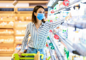 Woman in medical mask shopping in supermarket taking milk