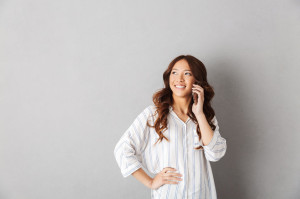 Cheerful asian woman standing isolated over gray