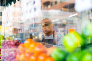 Supermarket worker in black apron putting vegetables in his department