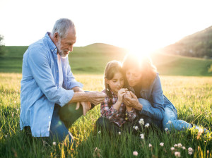 Senior couple with granddaughter outside in spring nature at sunset.