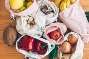 Fresh groceries in eco cotton bags on wooden table, flat lay. Ze