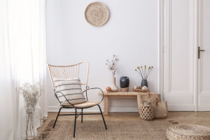 Flowers on wooden stool next to armchair in white loft interior with pouf and plate. Real photo