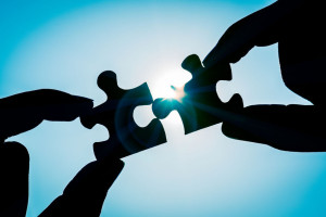 Silhouette of closeup woman's hand connecting a piece of jigsaw