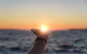 Hand reaches for the sun at sunset.